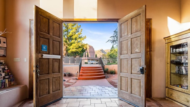 A hotel entrance with wooden doors, a stone pathway, and a view of a mountain landscape. - Adobe Village Inn Painted Desert (Sedona)