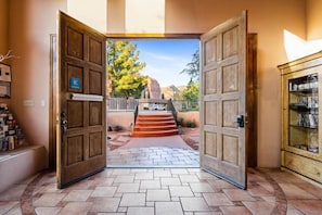 Entrada de hotel con puertas de madera, un sendero de piedra y vistas a un paisaje montañoso.