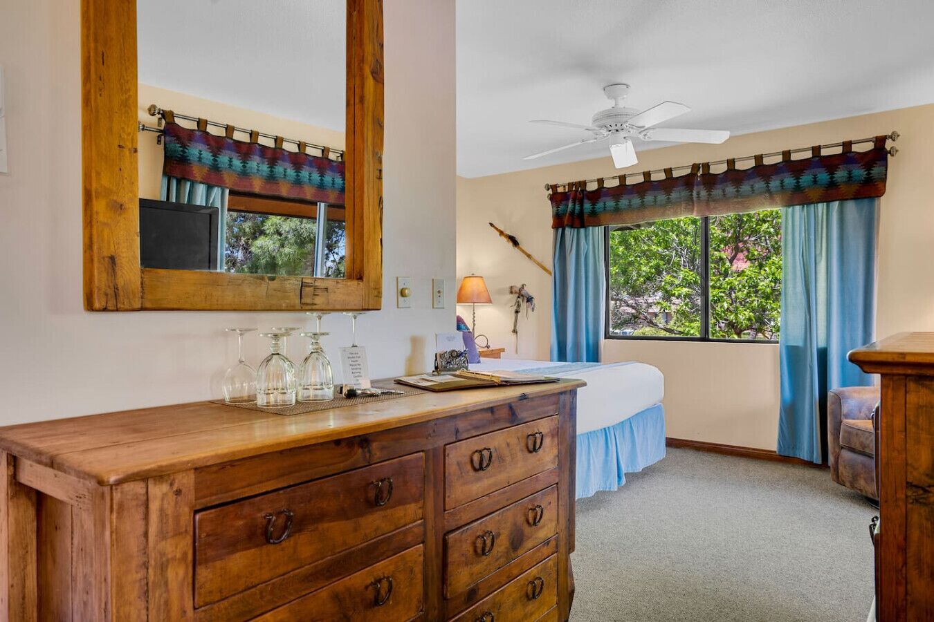 Quarto com cómoda de madeira, cama, ventoinha no teto e janela com cortinas.