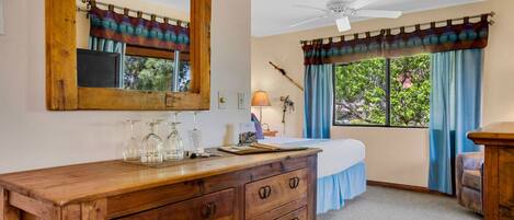 Quarto com cómoda de madeira, cama, ventoinha no teto e janela com cortinas.