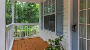 A covered porch with a wooden floor, white railings, a potted plant, and a door with a keypad lock.