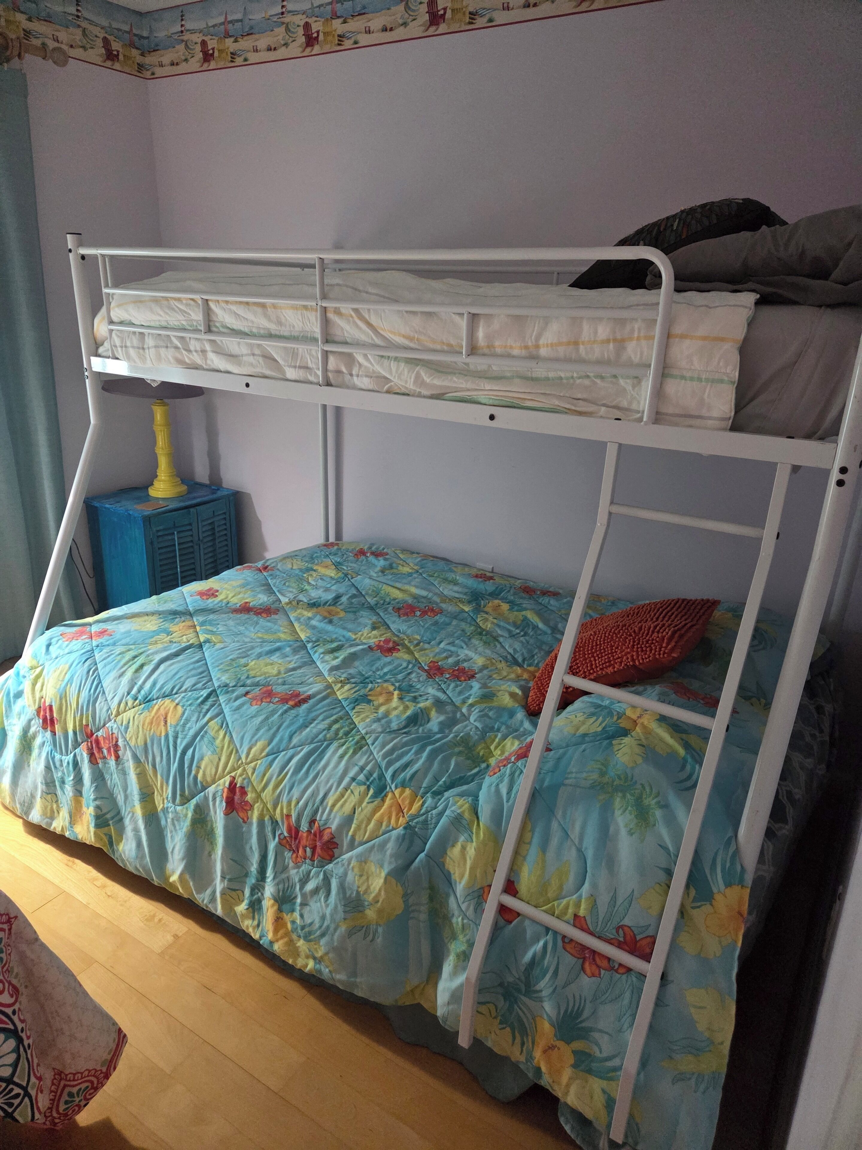 A bunk bed with a floral bedspread, a small blue stool, and a wall with a patterned border.