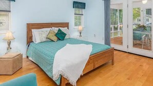 A bedroom with a wooden bed, a ceiling fan, and a view through a sliding glass door.