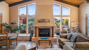 A living room with a fireplace, large windows, and a dining area with chairs and a table.