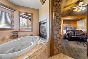 A bathroom with a large bathtub, a stone wall, and a wooden ceiling. - Adobe Village Inn Sundance Suite (Sedona)