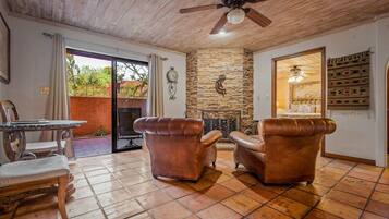 A room with a stone fireplace, leather armchairs, a dining table with chairs, and a ceiling fan.