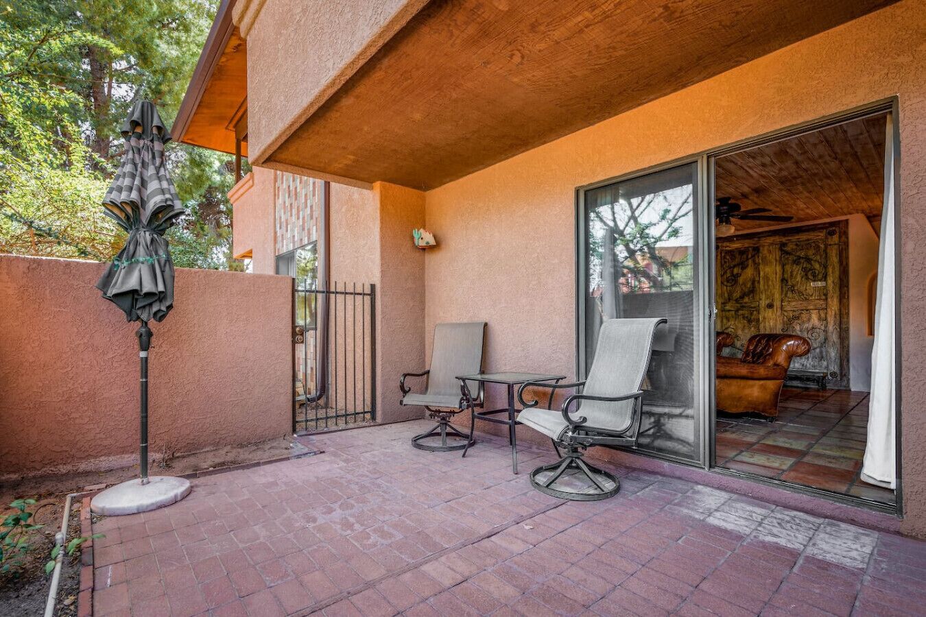 A patio with two chairs and a table, a covered area, and a sliding glass door leading to an interior space with a chair.