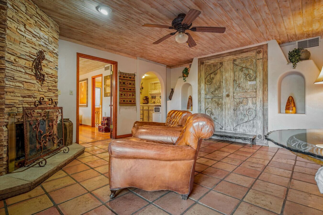 A spacious living area with a leather sofa, a stone wall, a wooden ceiling fan, and a rustic door.