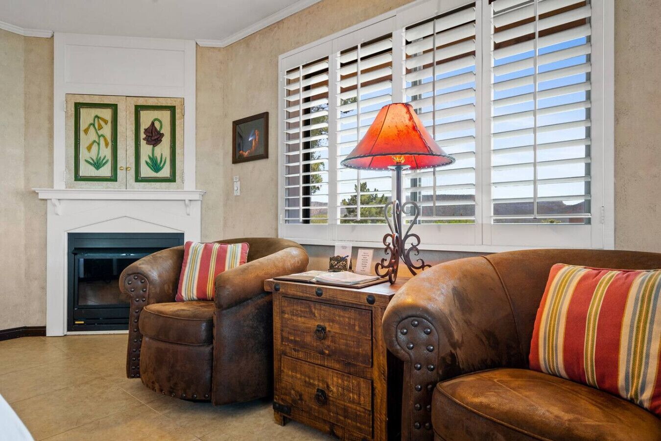 A living room with a fireplace, leather sofas, a wooden side table, and a window with blinds.