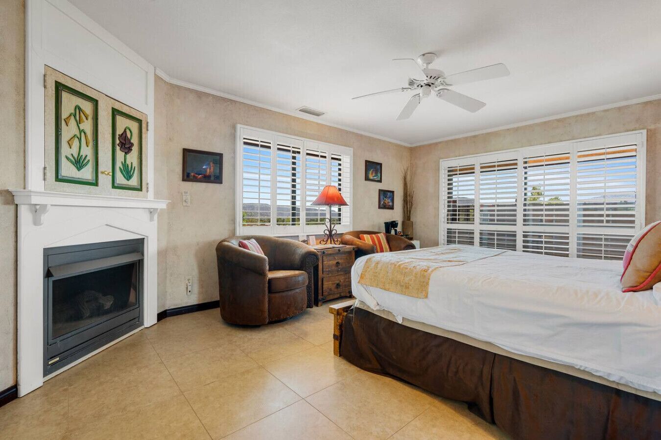 Une chambre à coucher avec une cheminée, un lit, une chaise, un bureau et un ventilateur de plafond.