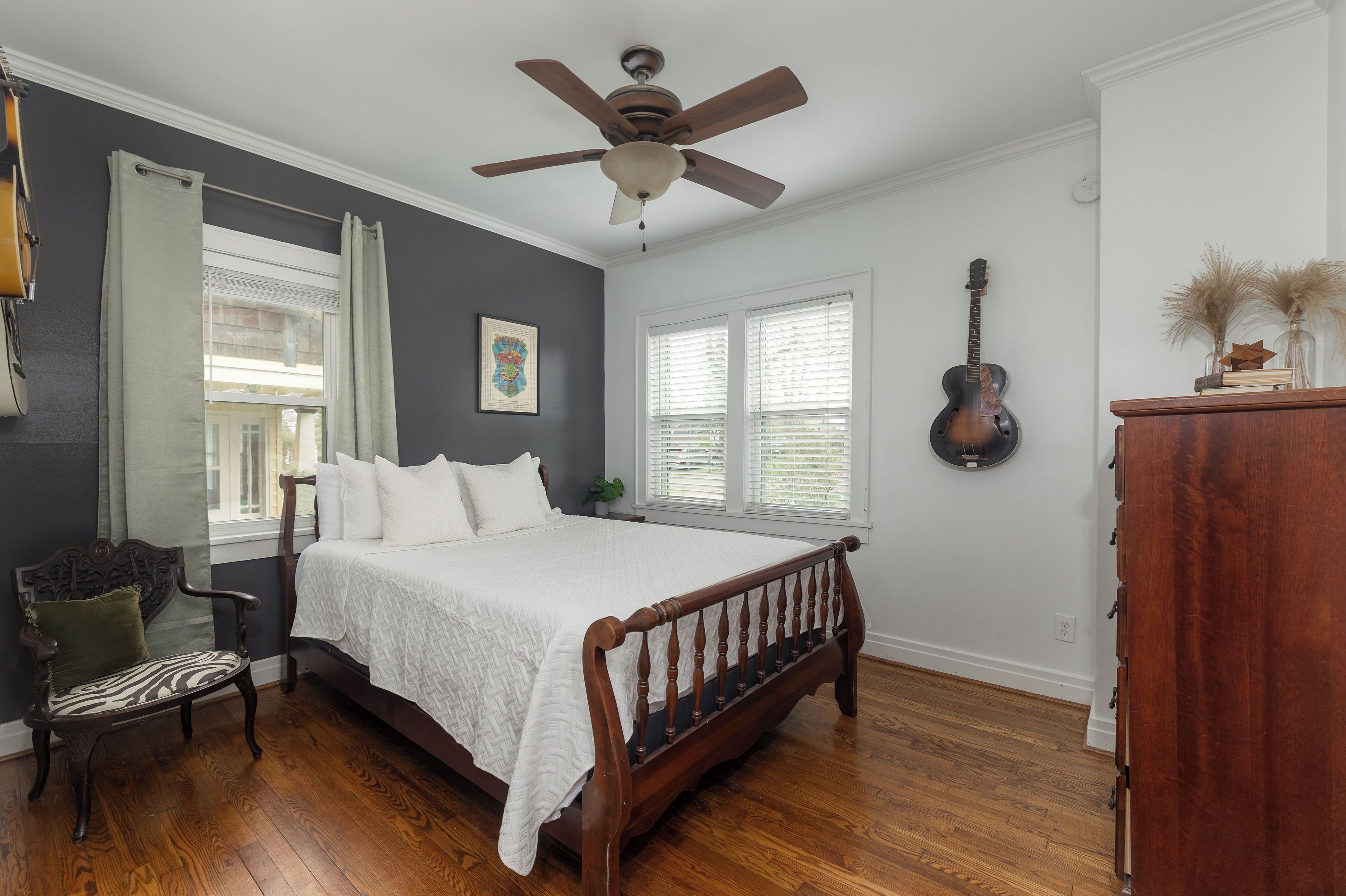 A bedroom with a bed, a ceiling fan, a guitar, and a dresser.