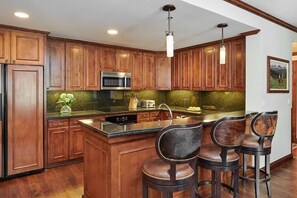 A kitchen with wooden cabinets, a stainless steel microwave, a large island with stools, and pendant lighting.