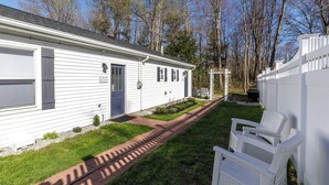 A single-story mobile home with a front porch, a small garden, and a white fence. - King Suite Getaway, Downtown Ogunquit. Walk to Beach, Shops & Dining! (Ogunquit)