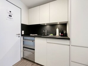 A compact kitchen with white cabinets, a black countertop, a stainless steel oven, and a sink. - Studio Phoenix - Zermatt by Interhome (Zermatt)