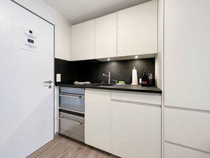 A compact kitchen with white cabinets, a black countertop, and stainless steel appliances. - Apartment  by Interhome (Zermatt)