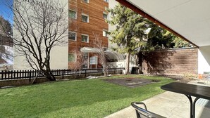 A courtyard with a grassy lawn, a metal table and chairs, and a building with a brick facade. - Apartment  by Interhome (Zermatt)