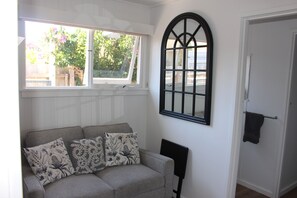 A room with a grey sofa, floral cushions, a black-framed window, and a white door. - beachside garden retreat 5 min walk to beach, cafe's, supermarket. (McCrae)