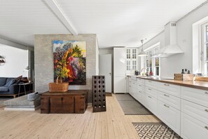 A modern kitchen with white cabinets, a large painting, and a wooden floor. - Cozy holiday home near the beach and Gilleleje (Gilleleje)
