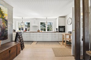 Et moderne køkken med hvide skabe, træbordplader, hængende lys og et stort vindue.