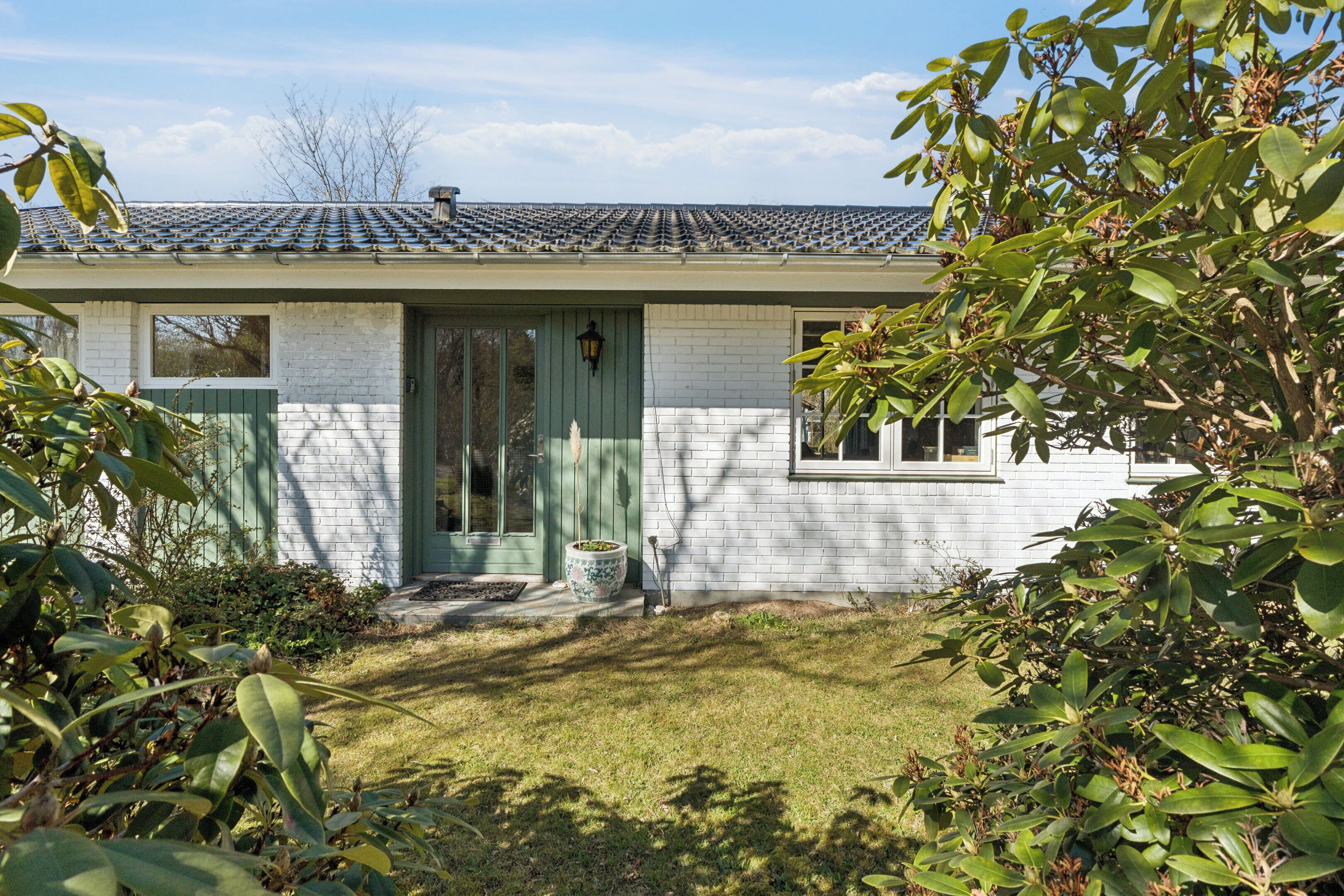 A house with a tiled roof, a green door, and a small front yard with a potted plant.