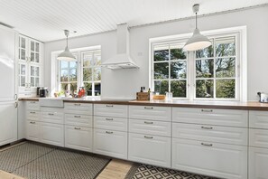 A modern kitchen with white cabinetry, a wooden countertop, pendant lights, and large windows. - Cozy holiday home near the beach and Gilleleje (Gilleleje)