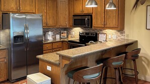 Una cocina con armarios de madera, electrodomésticos de acero inoxidable, encimera de granito y taburetes de bar.