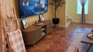 Una sala de estar con televisor, un cuadro sobre caballete, una planta en maceta y suelo de baldosas.