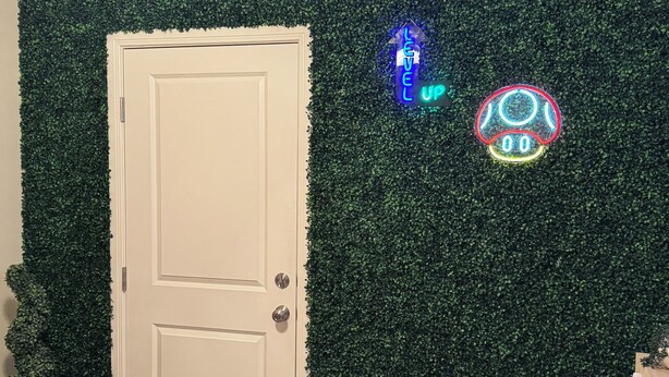 Una habitación con pared verde, una puerta blanca y dos letreros de neón.