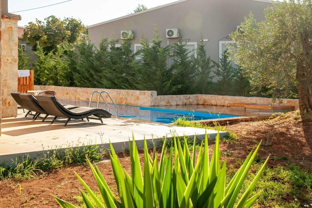 A swimming pool with lounge chairs, a concrete deck, and a building with air conditioning units in the background.