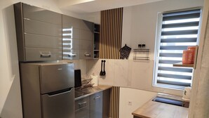 A modern kitchen with a stainless steel refrigerator, wooden accents, and a window with blinds.