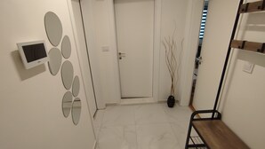 A hallway with a white door, a small screen, decorative wall mirrors, a potted plant, and a wooden bench.