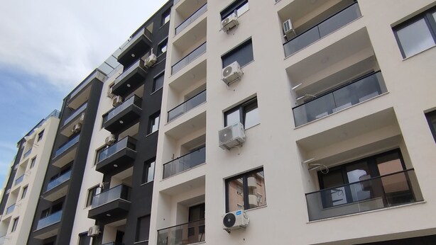 A multi-story residential building with balconies, air conditioning units, and a paved ground floor.