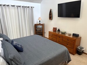 Un dormitorio con cama, cómoda, televisor y lámpara.