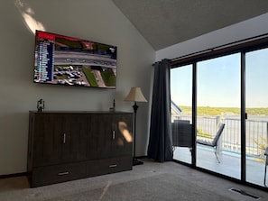 Habitación con televisión mostrando un evento de carreras, un aparador de madera, una lámpara y un balcón con vistas.