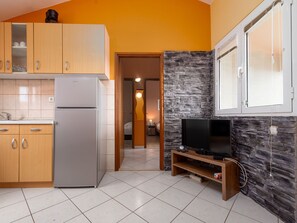 A compact kitchen with a refrigerator, wooden cabinets, and a stone accent wall. - Apartment  by Interhome (Biograd na Moru)