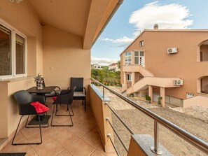 A balcony with a table and chairs, a potted plant, and a view of neighboring buildings. - Apartment  by Interhome (Biograd na Moru)