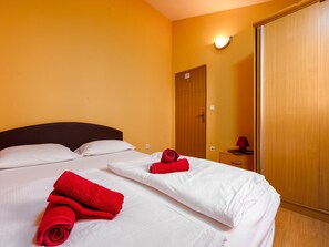 A hotel room with two beds, each with white linens and red towels. There is a wooden wardrobe and a bedside table with a lamp. - Apartment Julia A1,  2+2 by Interhome (Biograd na Moru)