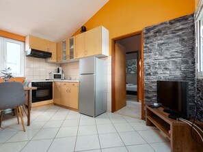 A modern kitchen with a refrigerator, microwave, and stove, leading to a living area with a television and stone wall. - Apartment  by Interhome (Biograd na Moru)
