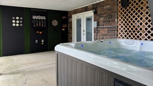 A hot tub with a control panel, dartboard, and a door labeled 'GAME ROOM' in a covered outdoor area. - La Buena Vida Retreat  Hot Tub • Game Room • Fire Pit (Huddleston)
