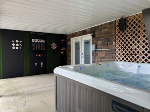 Ein Whirlpool mit Bedienfeld, eine Dartscheibe und eine Tür mit der Aufschrift 'GAME ROOM' in einem überdachten Außenbereich.