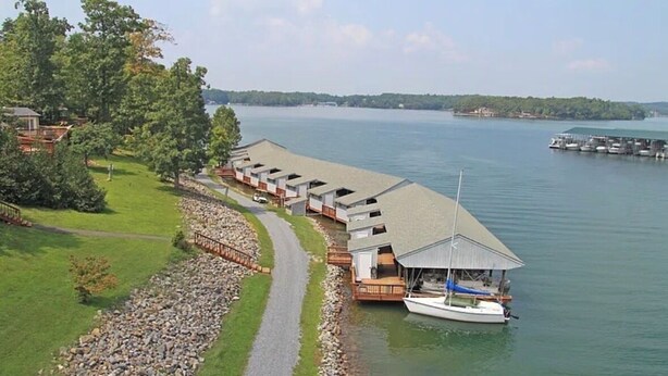 A lakeside lodge with a dock, a covered boat launch, and a pathway leading to the buildings. - La Buena Vida Retreat  Hot Tub • Game Room  • Fire Pit (Huddleston)