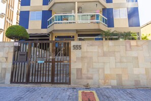 A multi-story building with a gated entrance, numbered 555, and a sign indicating 'ENTREGAS' (deliveries). - Apto a 750m da Praia da Enseada com Ar e Wi-fi (Guarujá)