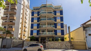 A multi-story building with balconies, a gated entrance, and a parked car in front. - Apto a 750m da Praia da Enseada com Ar e Wi-fi (Guarujá)