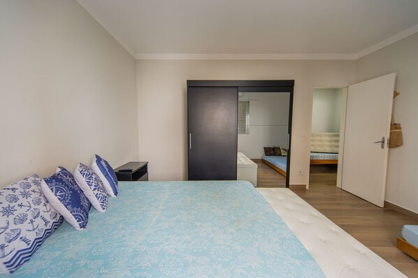 A bedroom with a bed, bedside tables, a wardrobe, and a mirror. - Apto a 750m da Praia da Enseada com Ar e Wi-fi (Guarujá)