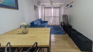 A living room with a sofa, TV, and a dining area with a table and chairs. - Apto a 750m da Praia da Enseada com Ar e Wi-fi (Guarujá)