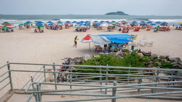 A beach with umbrellas, chairs, and a metal railing. - Apto a 750m da Praia da Enseada com Ar e Wi-fi (Guarujá)
