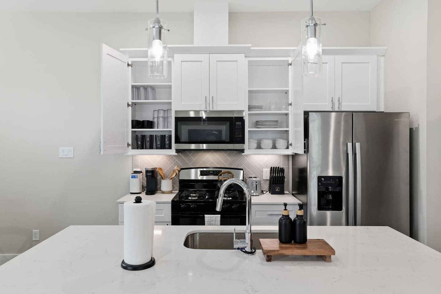 A modern kitchen with white cabinets, a stainless steel refrigerator, a microwave, and a stove.