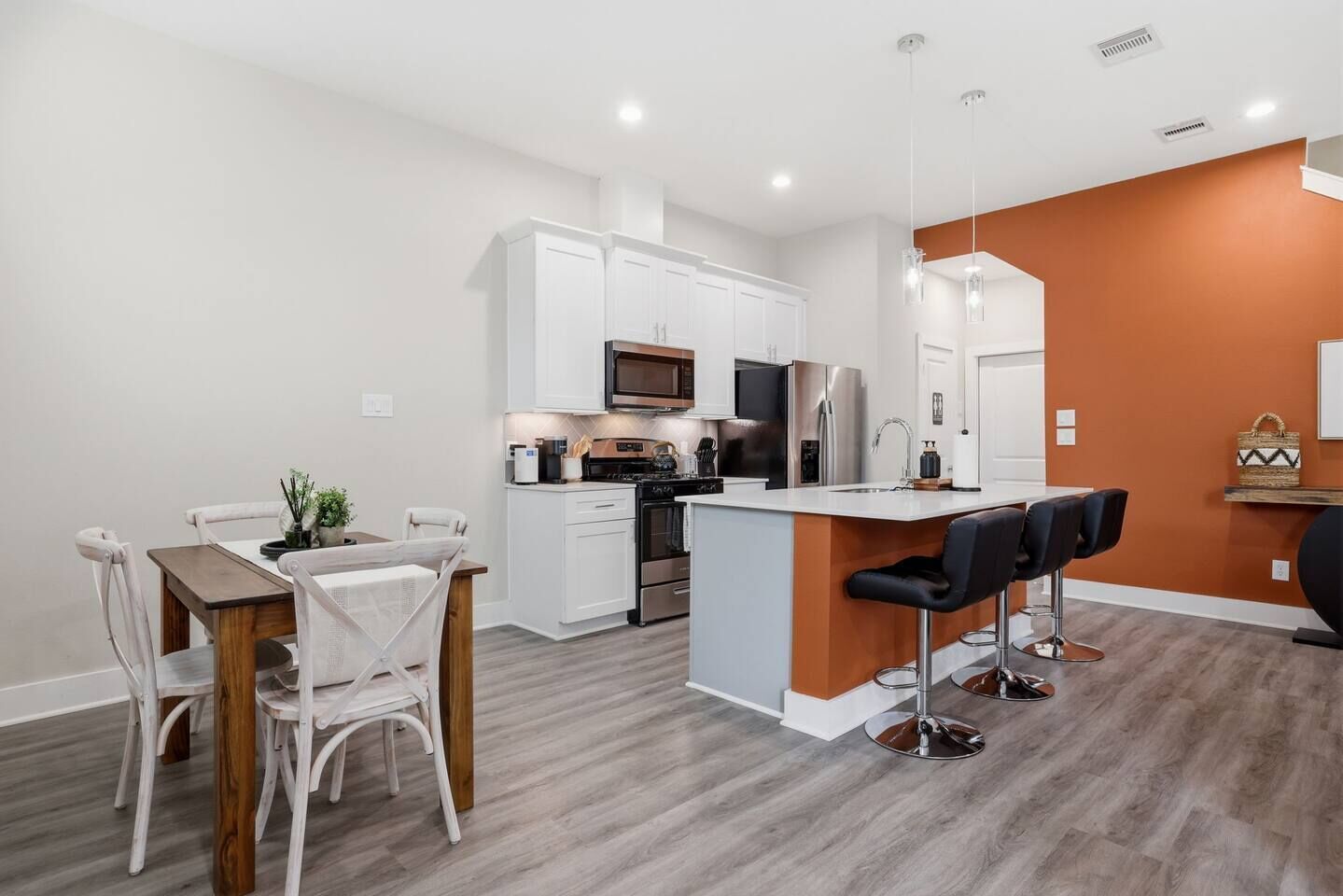 Una cocina moderna con armarios blancos, electrodomésticos de acero inoxidable y una isla central con taburetes de bar.