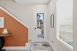 Ein Flur mit einer zur Gartenführenden Tür, einer Treppe, einem kleinen Teppich und einem an der Wand hängenden Bild.
