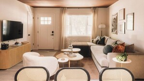 Ein gemütlicher Wohnbereich mit Sofa, zwei Sesseln, einem Couchtisch, Fernseher und einem Nachttisch mit Lampe.